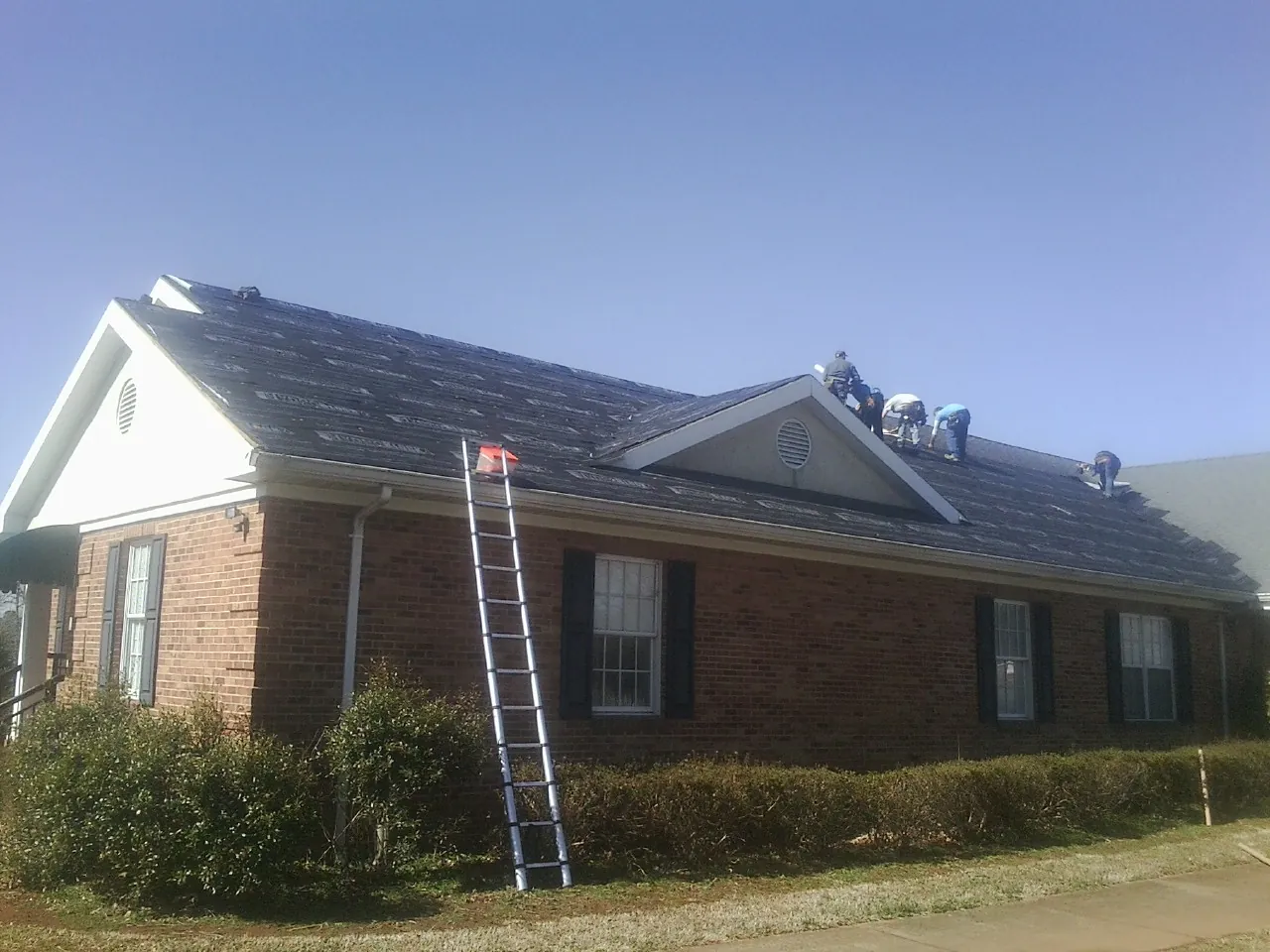 Crew tearing shingles off a brick ranch roof with a ladder set — Metal Roof Repair work by our crew in Sassamansville