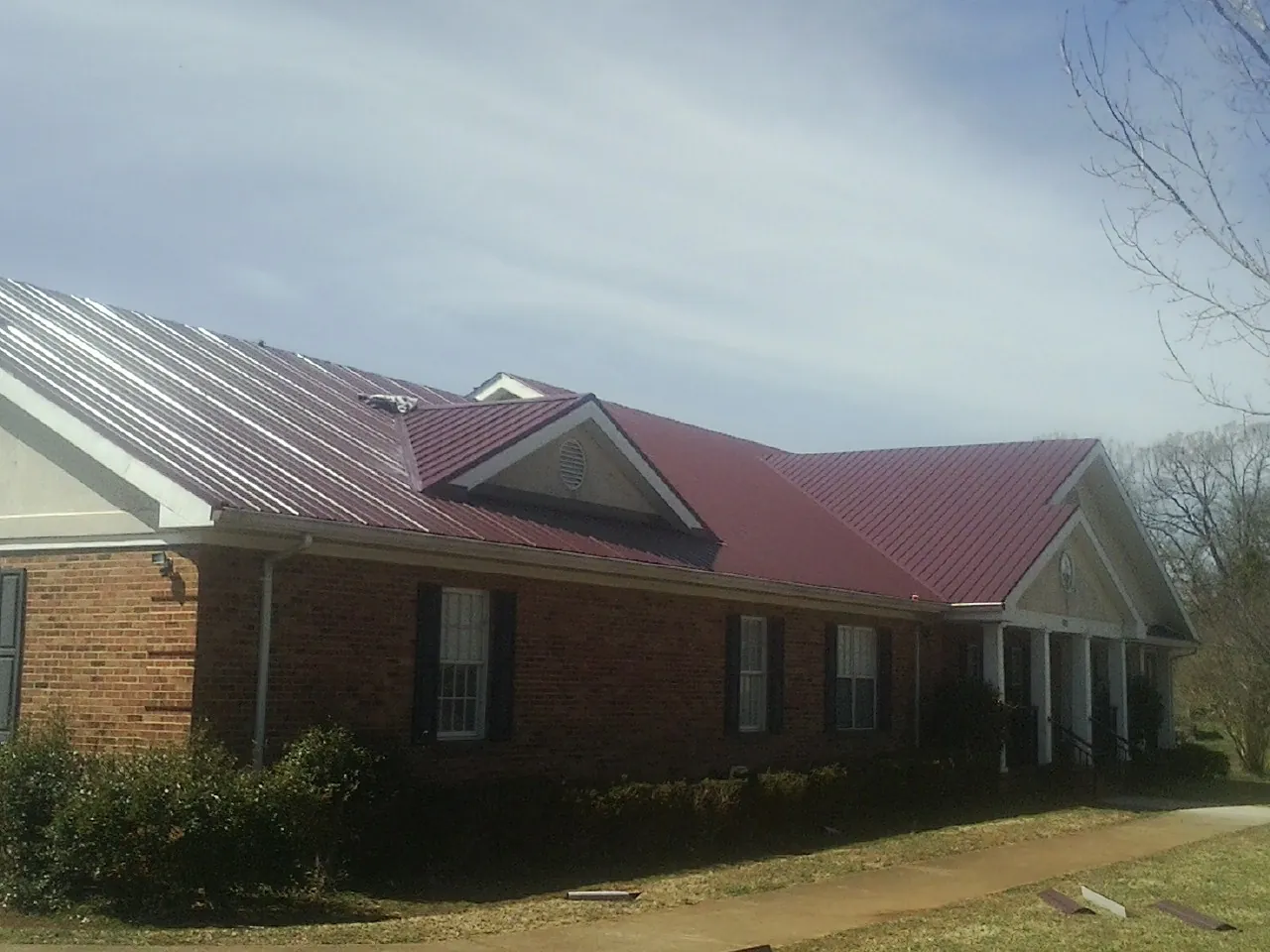 Red metal roof with gabled entries on a long brick building, from a Hail Damage Roof Repair job in Sassamansville