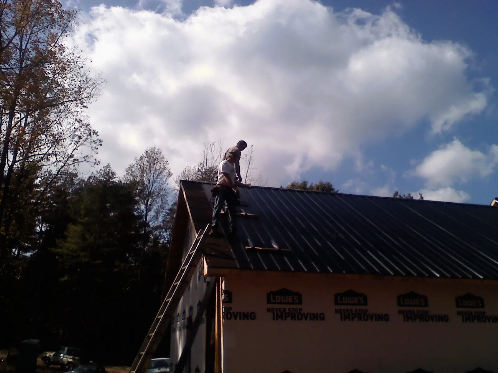 Roofer fastening dark metal panels high against a cloudy sky, from a Roof Inspection job in Sassamansville