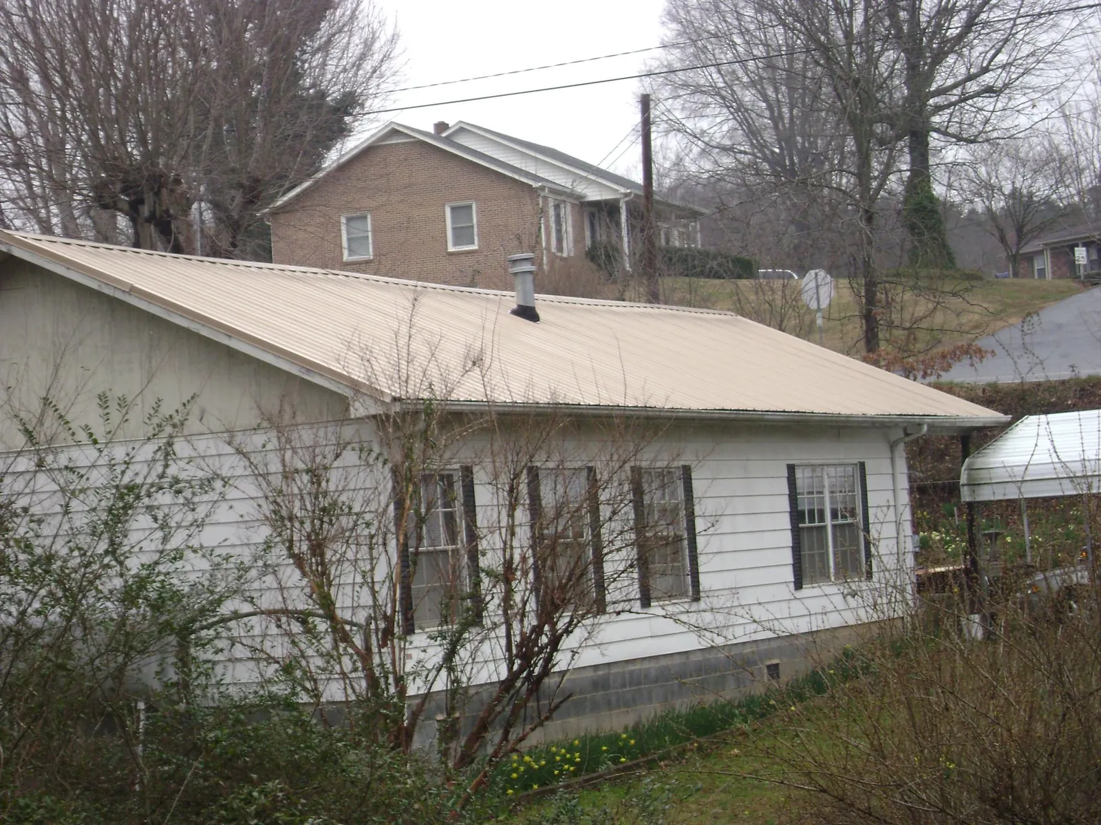 Tan metal roof on a white sided house set into a hillside — Commercial Roofing by Roofing Brothers in Sassamansville